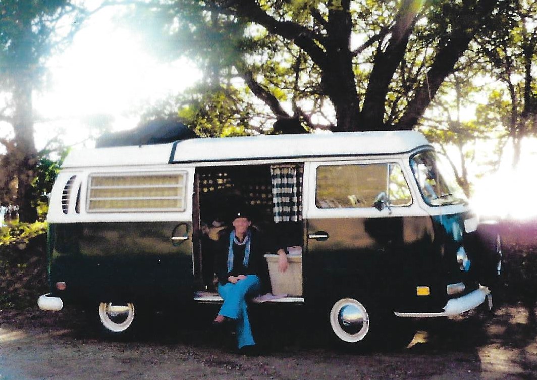 A woman sitting in the doorway of an old van.