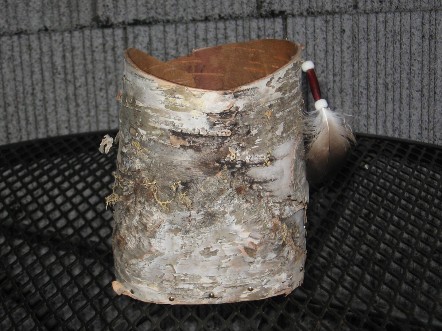 A small birch bark vase with a feather on top.