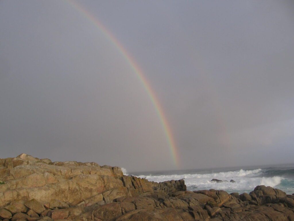 A rainbow over the ocean and rocks on the beach.