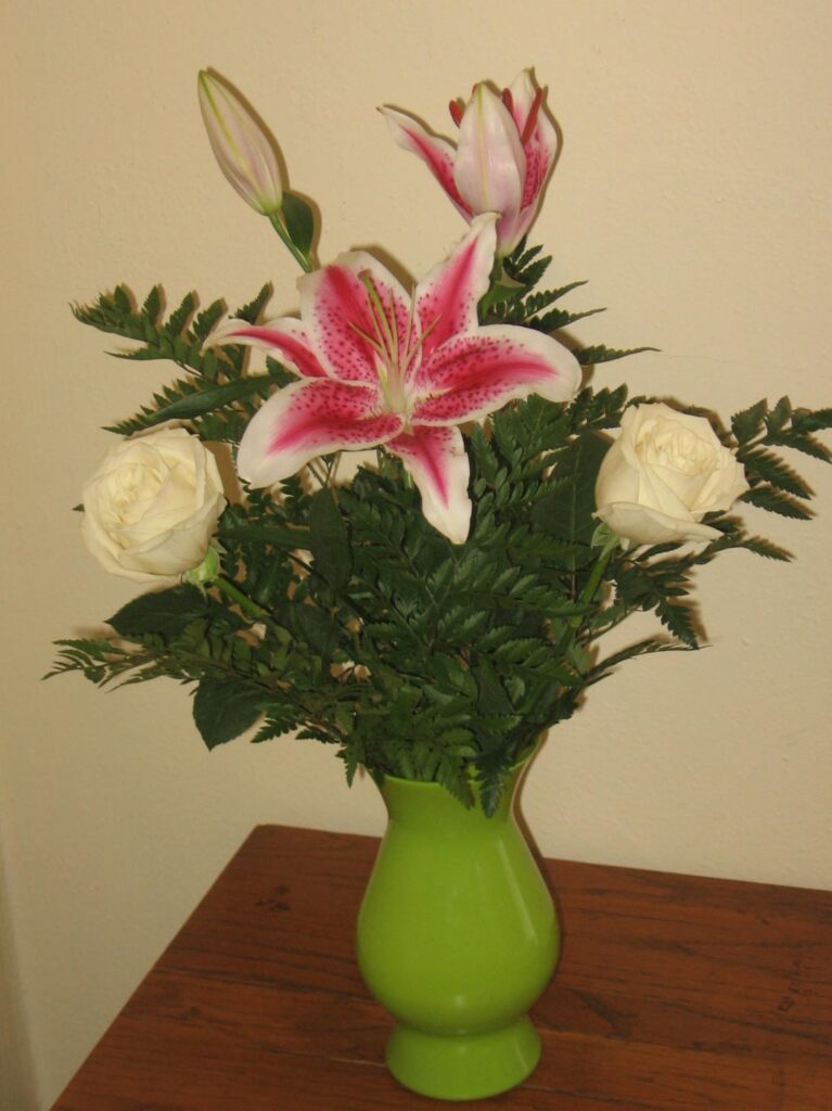 A green vase with flowers on top of a table.