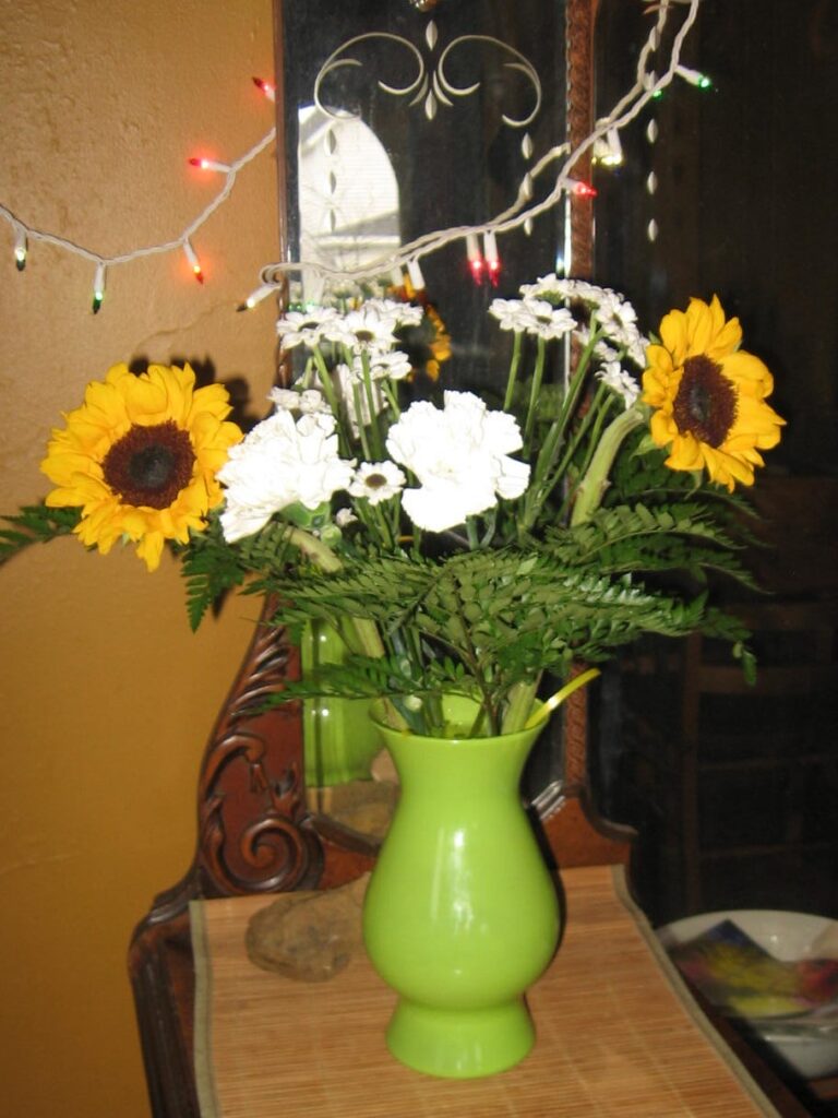 A green vase with flowers on top of a table.