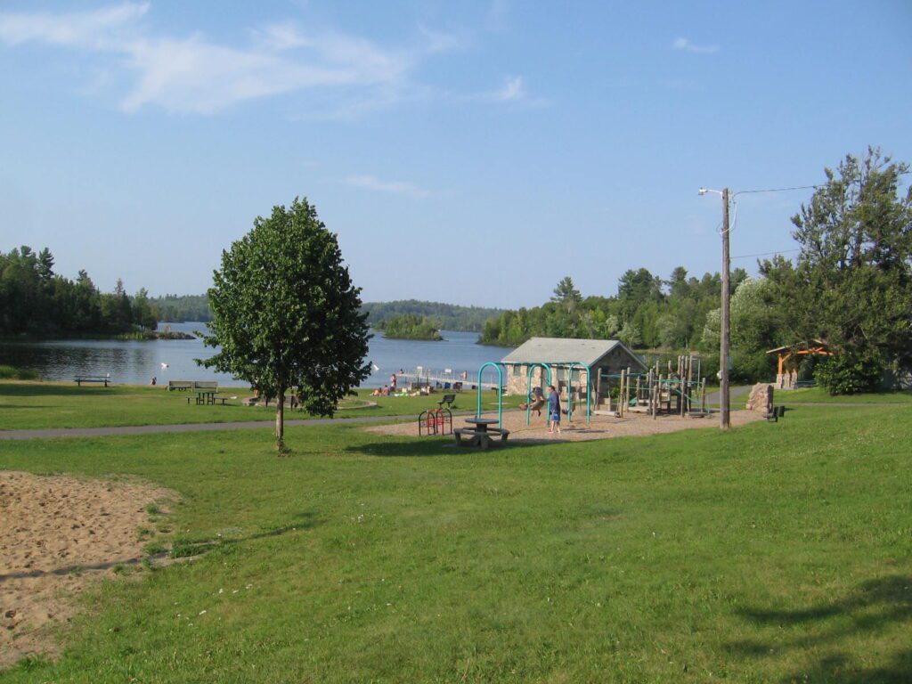 A grassy area with trees and houses near the water.