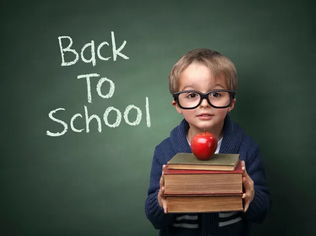 A boy holding books and an apple in front of a chalkboard.