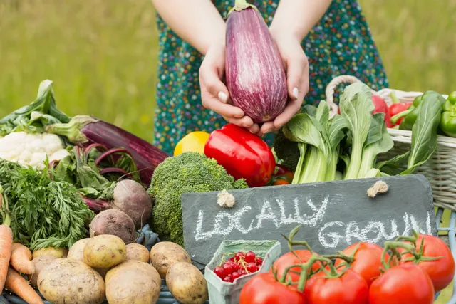 A woman holding an onion in front of vegetables.