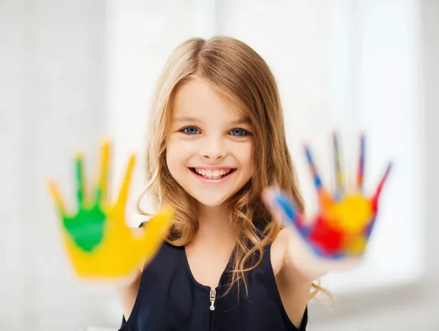 A little girl with long hair and a black top is holding up her hands