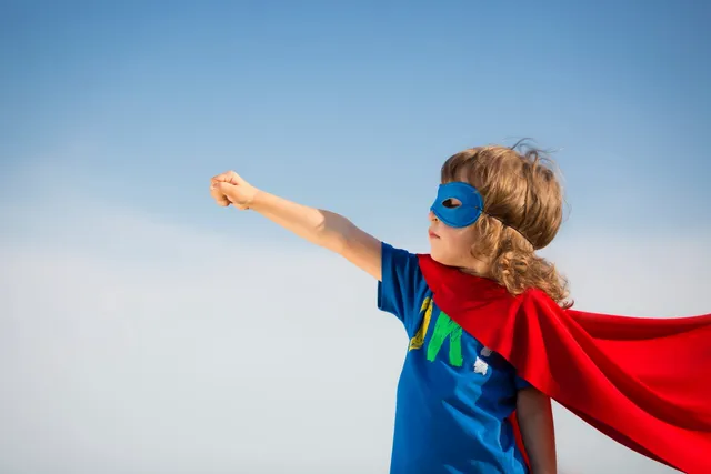 A young child dressed as superman with a cape and mask.