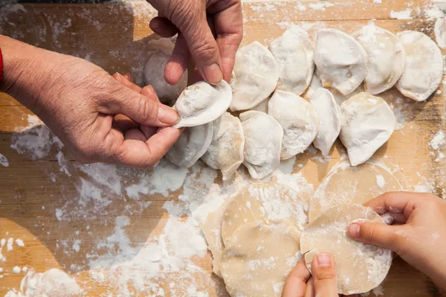 A group of people making dumplings on top of a table.