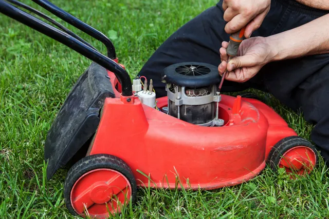 A person is fixing the motor on a red lawnmower.