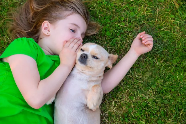 A little girl laying on the grass with her dog.