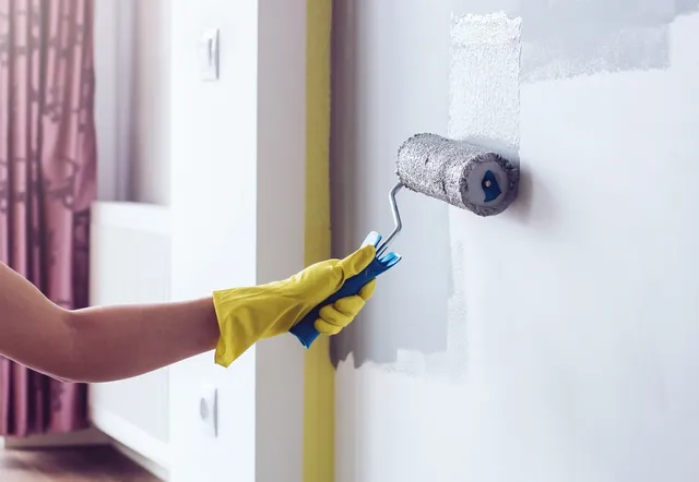 A person painting the wall with paint roller.