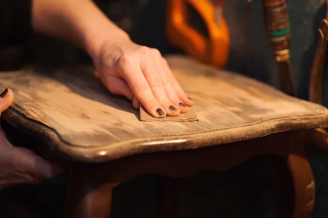 A person is using a sanding block on a wooden table.