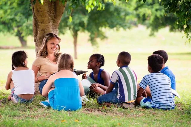 A group of children sitting around under a tree.