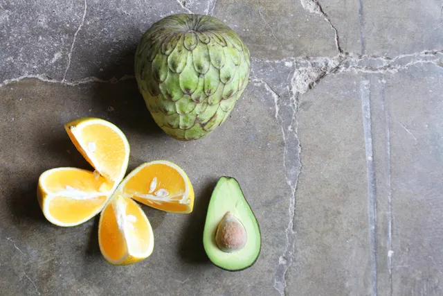 An orange, a pineapple and an avocado on the table.