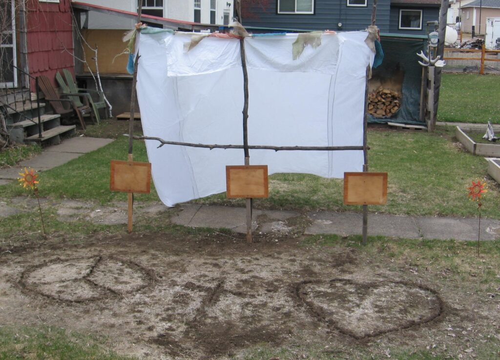 A dirty field with three wooden boards and some clothes hanging on it.